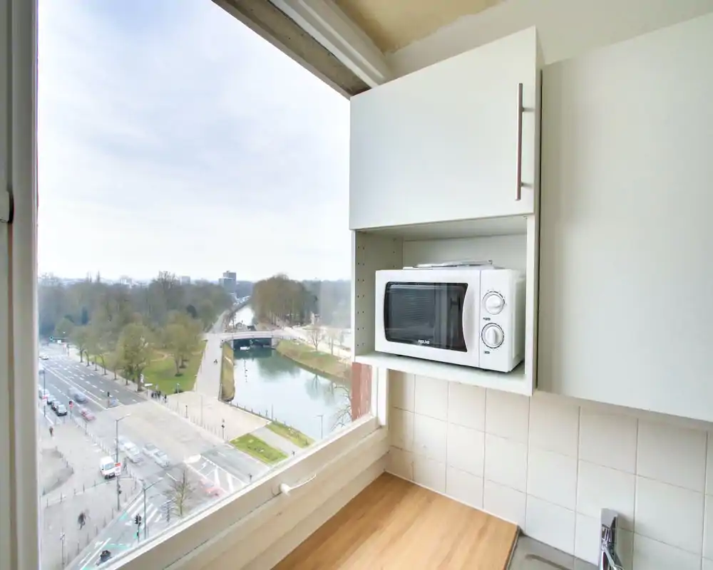 Compact kitchen corner with a built-in microwave, clean white cabinets, wooden countertop and a large window offering a canal and park view.