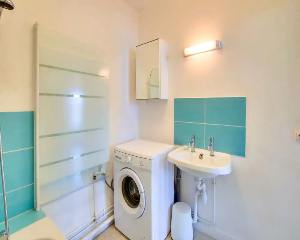 Compact bathroom with a sink, wall-mounted mirror cabinet and a washing machine beside it; turquoise tile accents add a fresh touch.