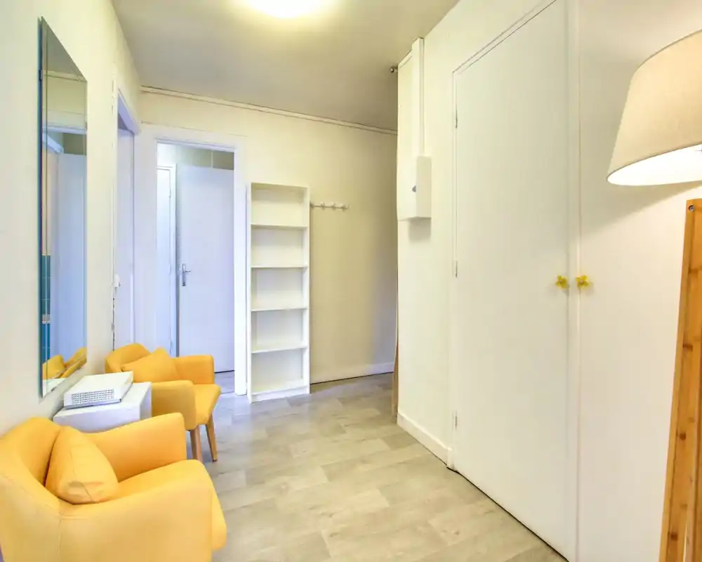 Bright, welcoming entrance area with two yellow armchairs, wall mirror and bookshelf — ideal as a small waiting area or foyer.