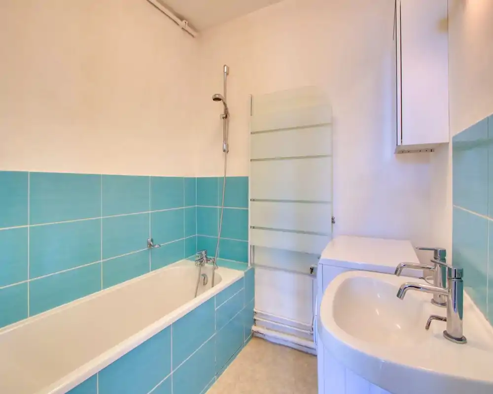 Clean, modern bathroom with a bathtub and wall-mounted showerhead, turquoise tiled lower walls, a white sink with chrome faucets and a heated towel radiator.