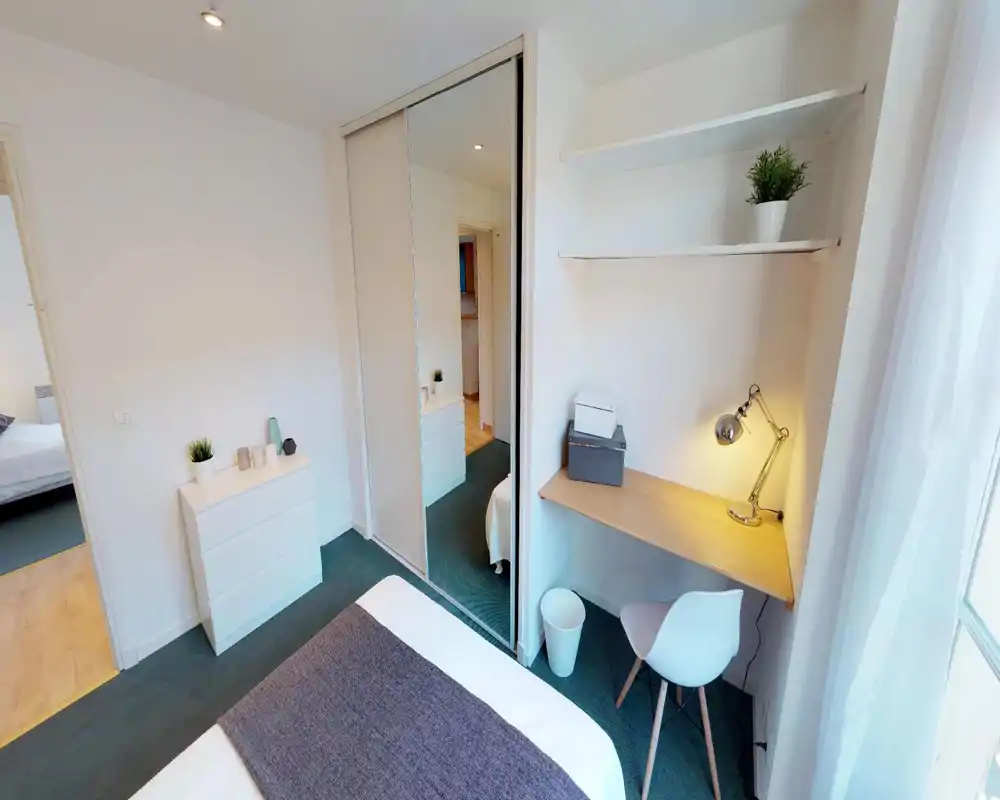 Camera da letto moderna e luminosa con letto comodo, armadio con specchio e un piccolo angolo studio vicino alla finestra — arredo pulito e luce naturale invitante.