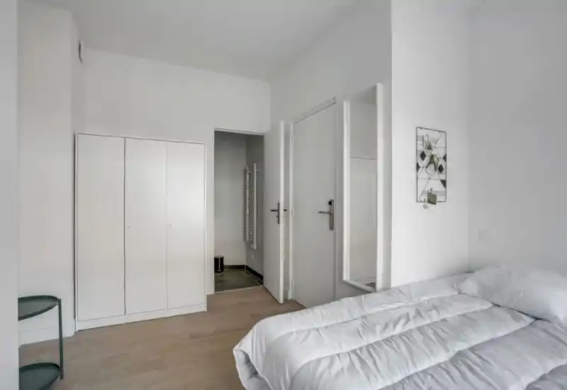 Camera da letto minimalista con letto matrimoniale bianco, biancheria semplice e armadio a muro; ambiente luminoso, pulito e ordinato ideale per annunci.