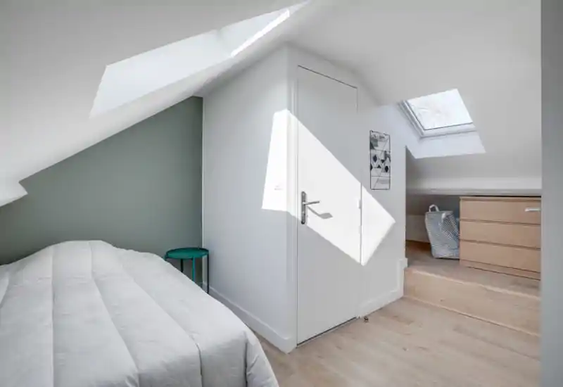 Camera da letto mansardata, luminosa e moderna con letto comodo, finestre a tetto e arredi minimal che creano un'atmosfera tranquilla e ariosa.