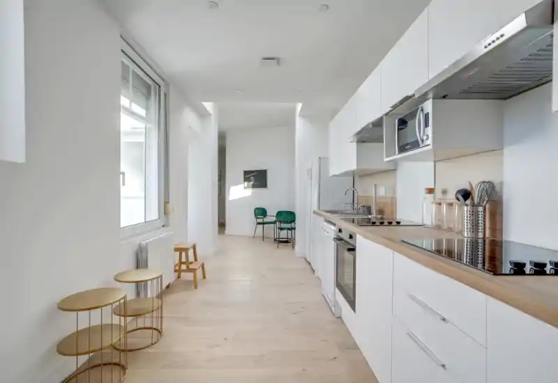 Bright, modern galley kitchen with white cabinets, wood countertop and integrated appliances; clean minimalist styling and natural light make it ideal for rental photos.