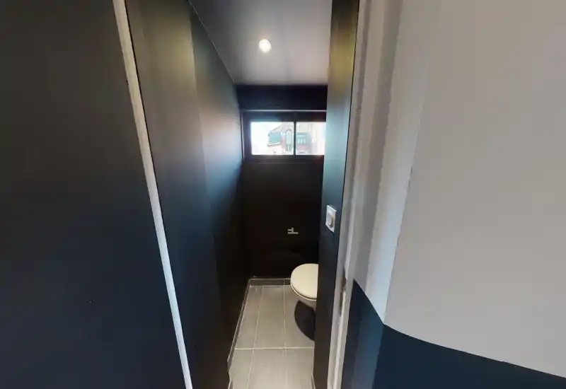 Compact, modern WC with dark walls, a wall-mounted toilet and a narrow high window providing daylight.