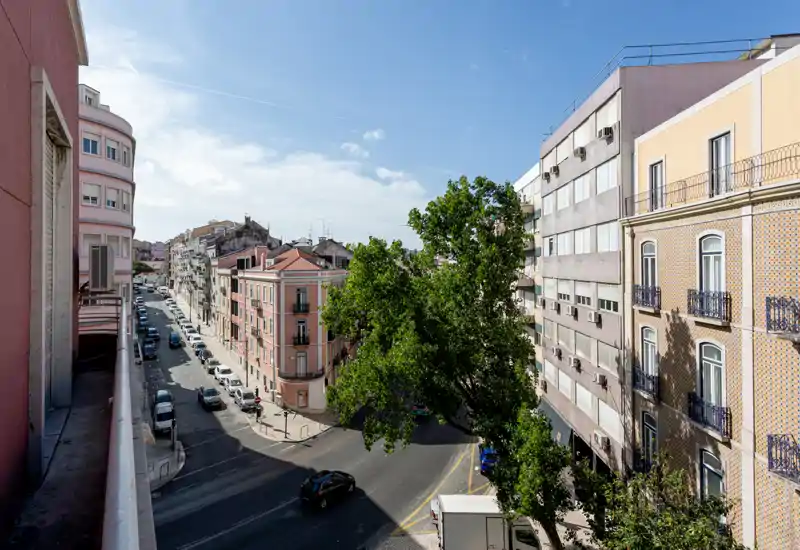 Sunny street view from a balcony overlooking a tree-lined intersection and classic urban buildings — ideal for showcasing location and nearby streets.