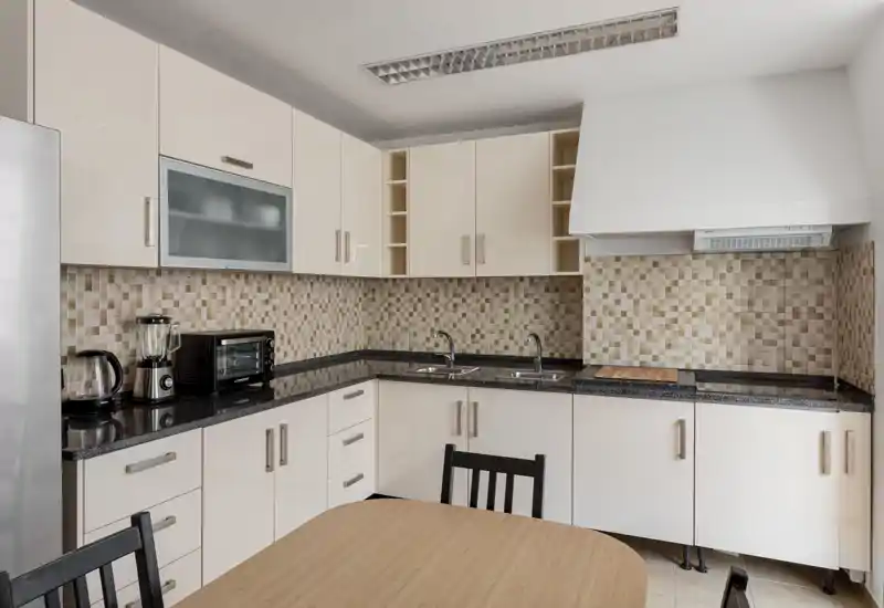 Bright, modern kitchen with L-shaped countertops, glossy cabinets, mosaic tile backsplash and integrated appliances — neat and ready for cooking.