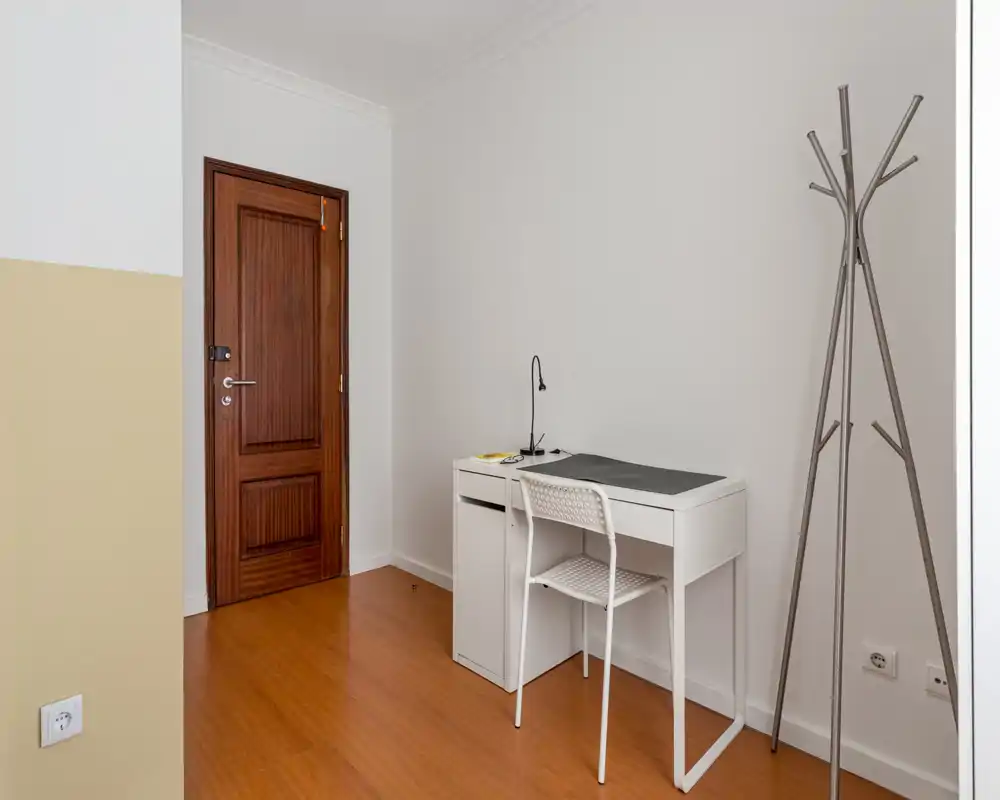 Petit hall d'entrée bien éclairé avec une porte en bois, un petit bureau blanc et une chaise pour des tâches rapides, ainsi qu'un porte-manteau moderne. Lignes épurées et couleurs neutres pour une première impression propre et fonctionnelle.
