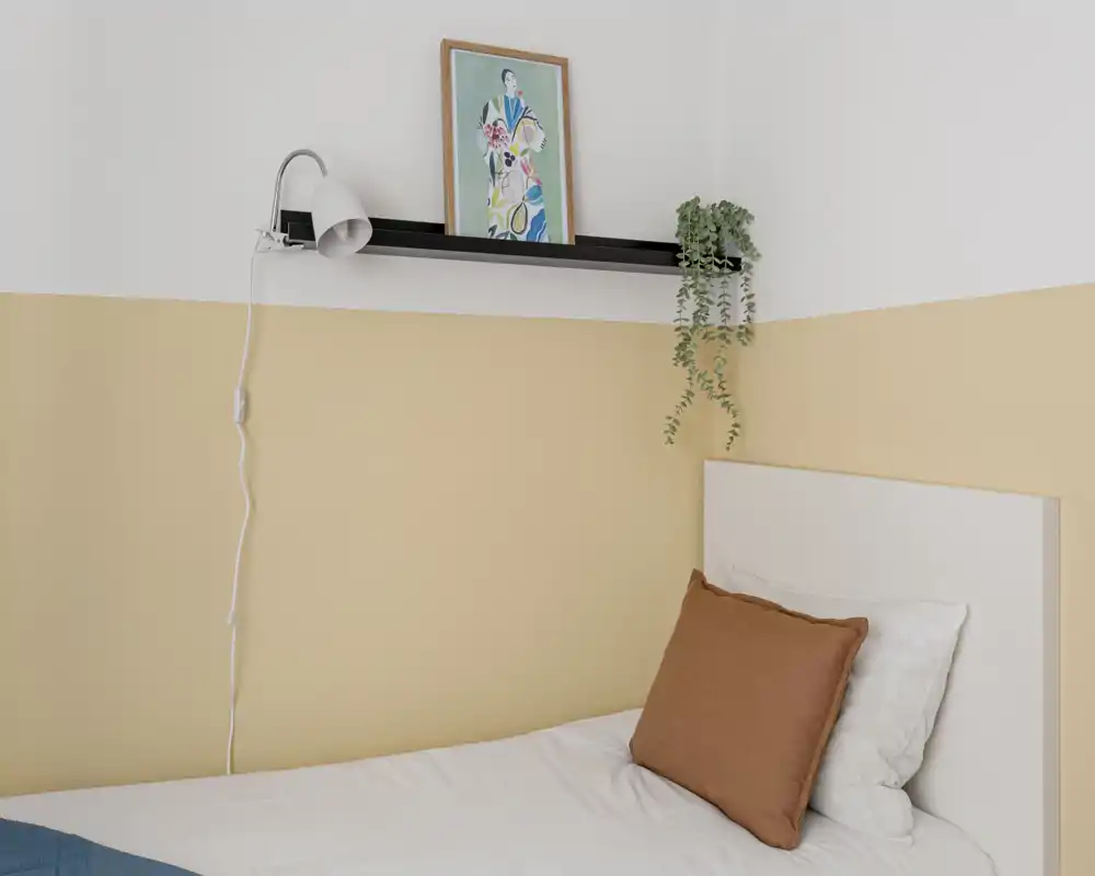 Coin chambre lumineux et minimaliste avec un lit simple bien fait, une tête de lit blanche, un mur beige chaud et une étagère décorative avec lampe et plante.