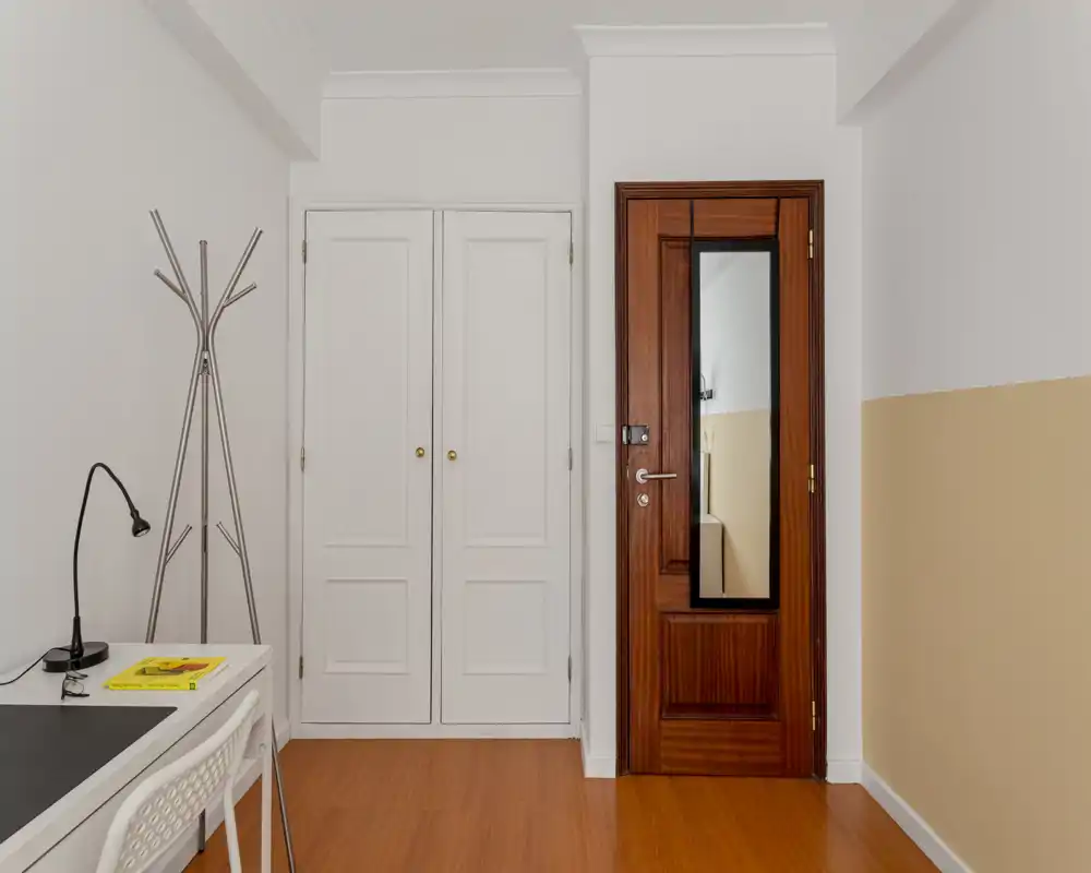 Entrée lumineuse et minimaliste avec porte en bois, placard mural blanc et petit bureau visible sur le côté — espace d'accueil simple et soigné.