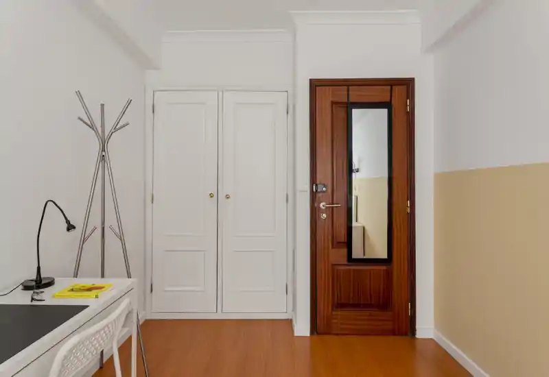 Entrée lumineuse et minimaliste avec porte en bois, placard mural blanc et petit bureau visible sur le côté — espace d'accueil simple et soigné.