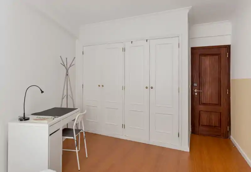 Coin de chambre minimaliste et lumineux avec placards intégrés blancs, un petit bureau et une porte en bois — espace pratique et épuré, adapté pour une personne ou un étudiant.