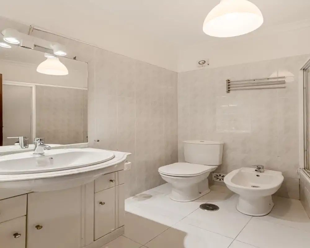 Salle de bains propre et carrelée avec lavabo, miroir, toilettes et bidet ; tons neutres et luminosité agréable, idéale pour les annonces locatives.