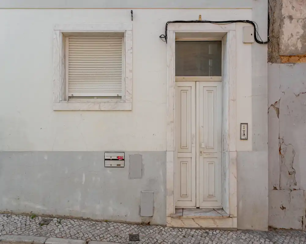 Façade au niveau de la rue montrant une porte d'entrée à panneaux, une fenêtre avec volet et une marche en pierre — utile comme photo extérieure pour une annonce.