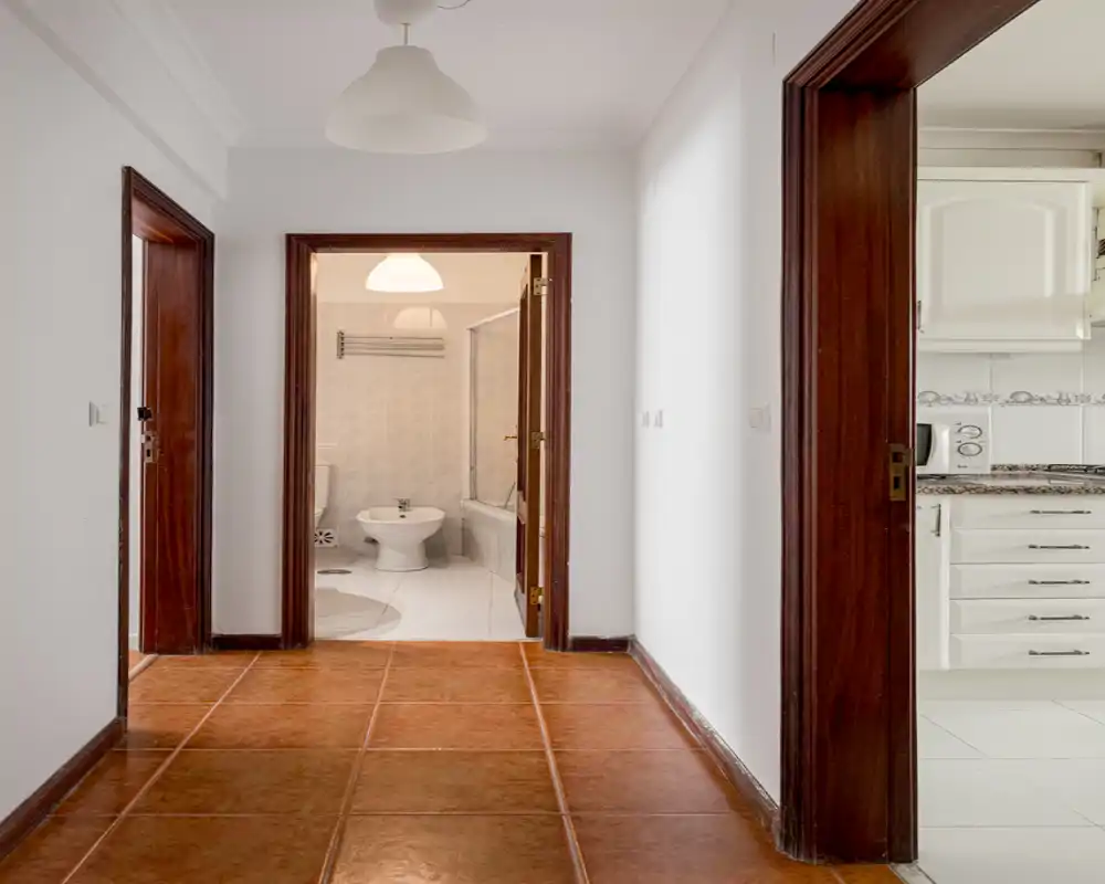 Entrée lumineuse avec carrelage terre cuite, murs blancs et portes visibles vers la salle de bain et la cuisine — espace propre et neutre prêt à être personnalisé.