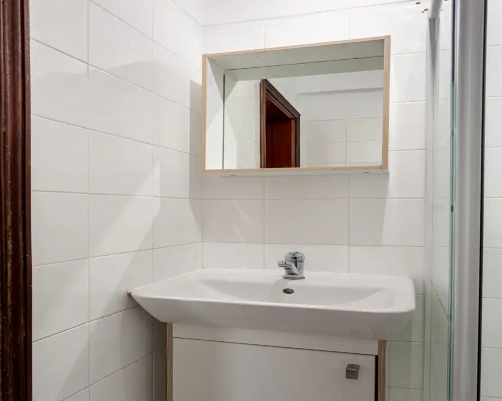 Salle de bain compacte et lumineuse avec lavabo mural, armoire miroir et murs carrelés — propre et fonctionnelle.