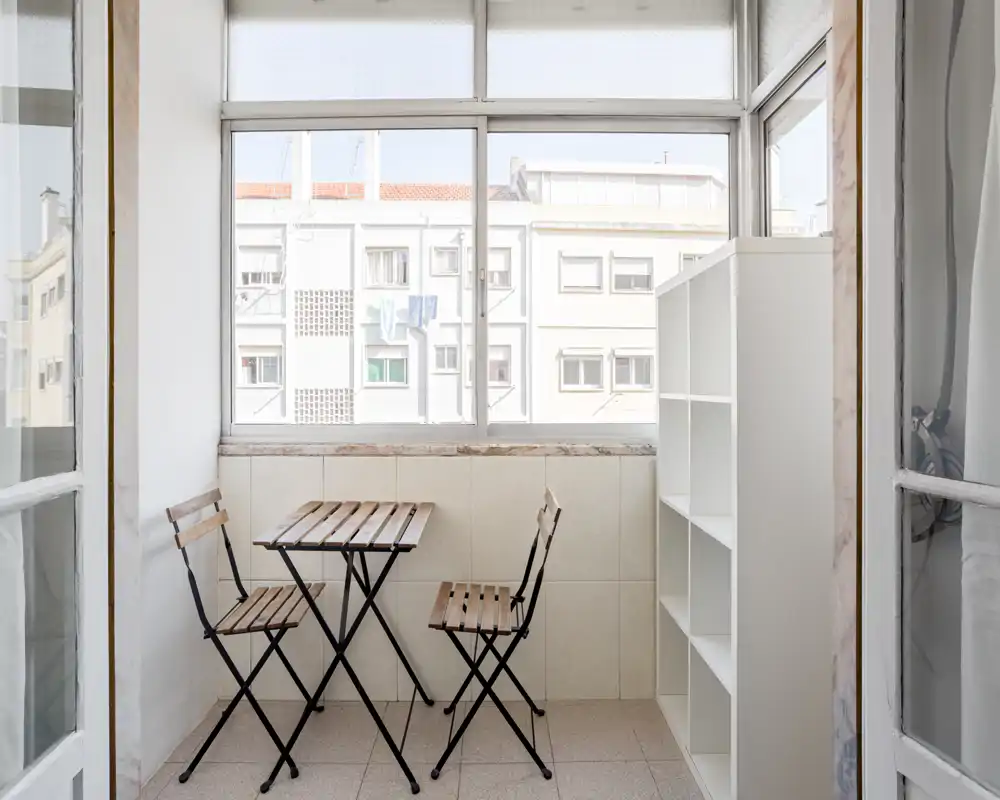 Bright enclosed balcony/terrace with a small wooden table and two folding chairs, ideal for morning coffee and enjoying city views.