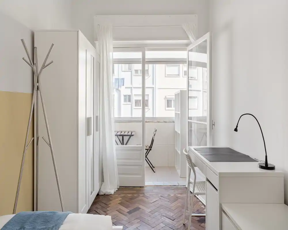 Bright, minimal bedroom with parquet floor, wardrobe, desk and a balcony letting in generous natural light.
