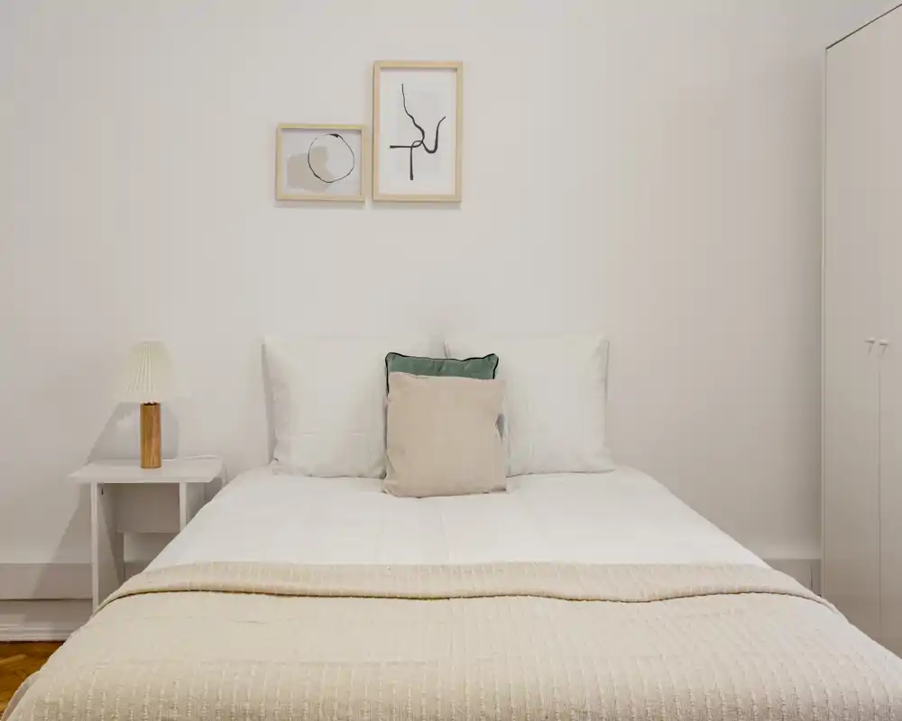 Bright, minimalist bedroom with a centrally placed double bed, soft neutral textiles and two framed artworks above the headboard; ideal for listing photos highlighting calm, modern styling.