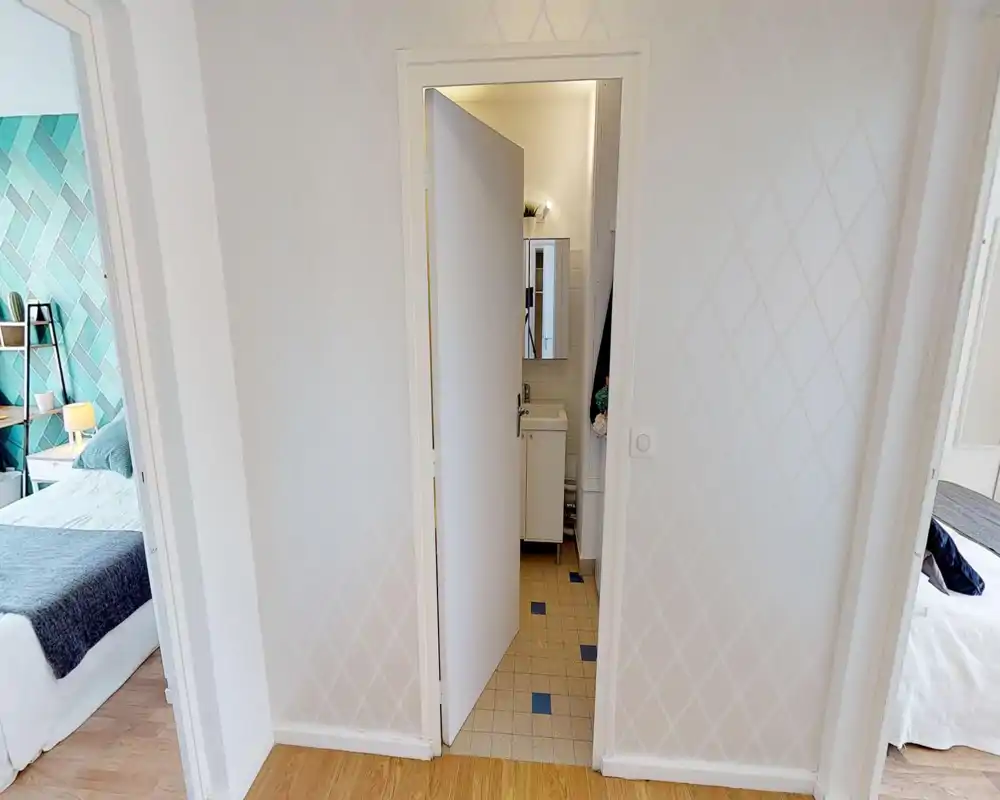 Petit hall d'entrée intérieur avec une porte centrale donnant sur la salle de bains ; sol en bois et murs à motif neutre, avec des ouvertures vers les chambres de chaque côté.