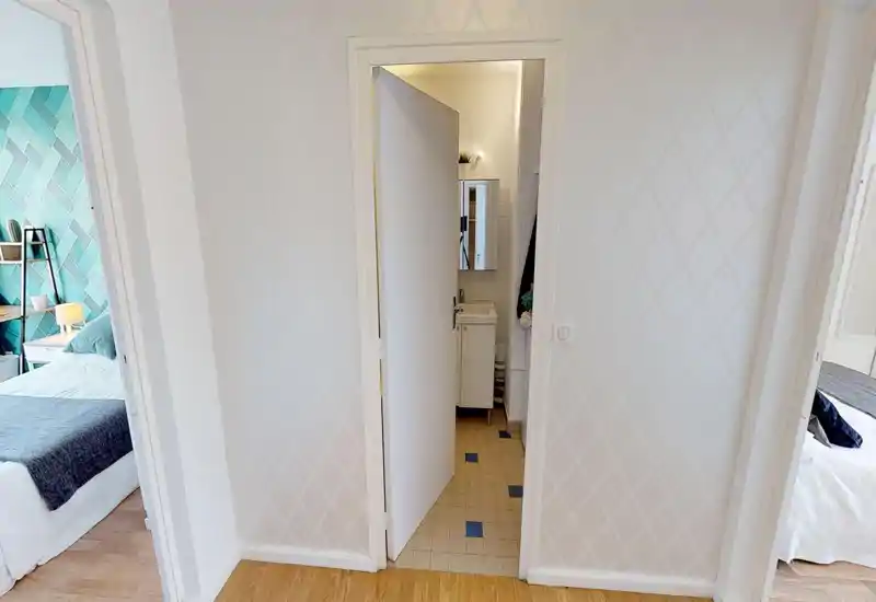 Piccolo ingresso/corridoio interno con porta centrale che conduce al bagno; pavimento in legno e pareti con motivo neutro, con aperture verso le camere da letto ai lati.