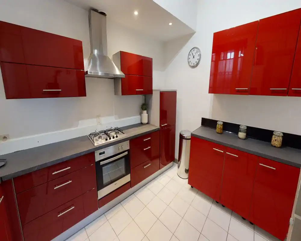 Modern kitchen with glossy red cabinets, gas hob and built-in oven. Bright, well organized workspace with countertop storage jars and a stainless steel extractor hood.
