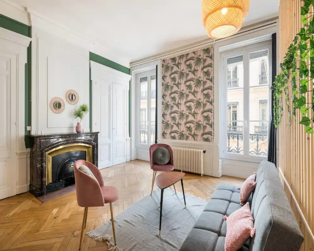 Sala de estar luminosa y con estilo con sofá gris, sillas rosas, chimenea decorativa y grandes ventanas que dejan entrar mucha luz natural.
