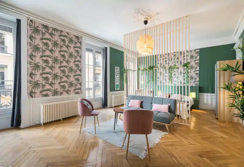 Stylish studio with a separated sleeping area: bright open living space with a cozy sofa, pink accent chairs and a bedroom cleverly screened by a wooden slatted divider.