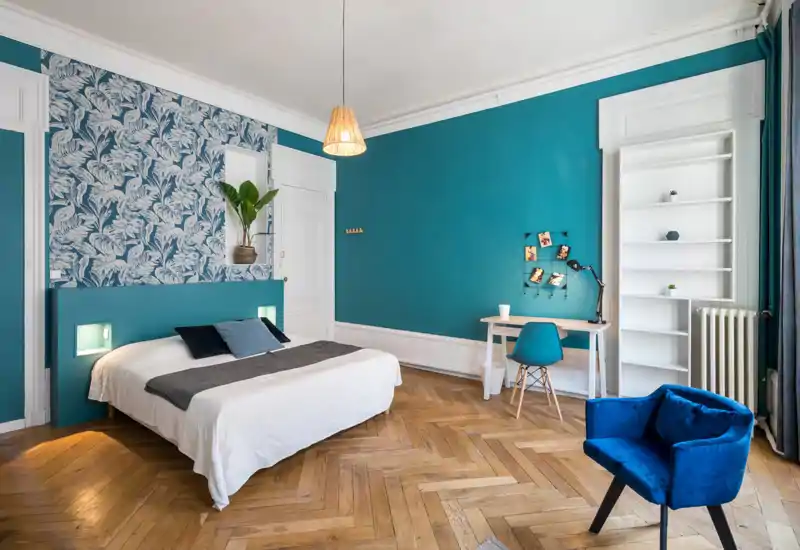 Dormitorio con estilo, cama doble completa, pared turquesa con papel pintado, suelo de madera en espiga, escritorio y butaca cómoda — luminoso, moderno y bien presentado para un anuncio.