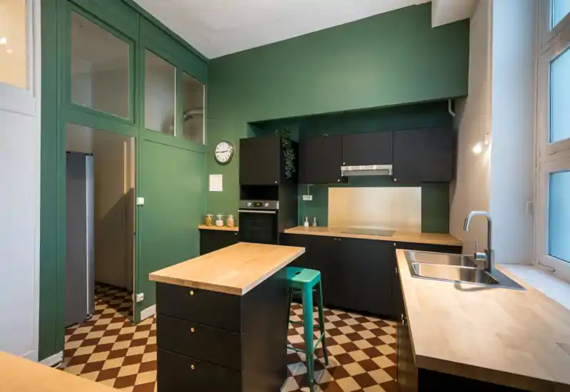 Cuisine moderne avec meubles foncés, plans de travail en bois clair et îlot central. Une grande fenêtre apporte de la lumière naturelle et le carrelage à motifs apporte du caractère.