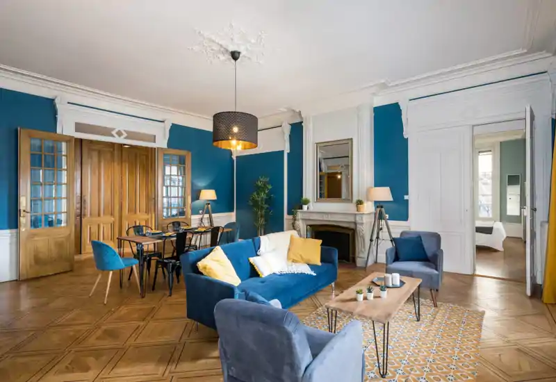 Soggiorno luminoso e di design con divano in velluto blu, poltrone, pavimento in parquet e camino decorativo — perfetto per momenti di relax e convivialità.
