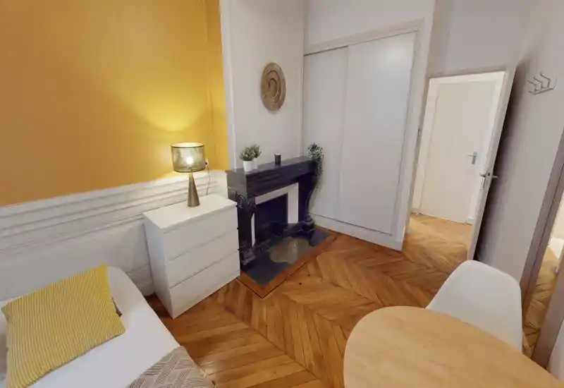 Stylish bedroom corner with warm yellow accent wall, a well-made single bed, bedside chest and decorative fireplace; bright, cozy and well-styled for a rental listing.