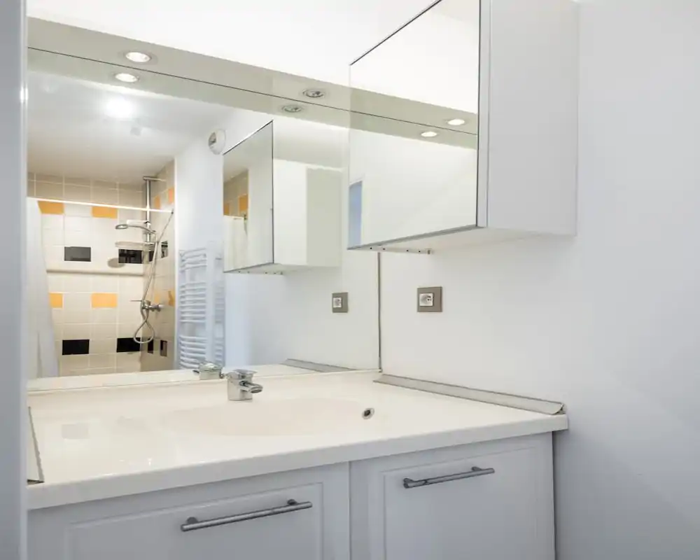 Bagno moderno e luminoso con lavabo bianco, specchiera con pensile e zona doccia piastrellata con accenti gialli e neri.