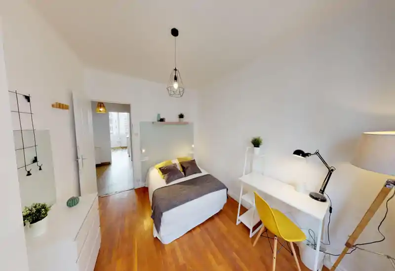 Bright, stylish bedroom with a centrally placed double bed, coordinated textiles and a small desk workspace. The room features warm wooden floors, bedside lights and tasteful decorative plants for a welcoming atmosphere.