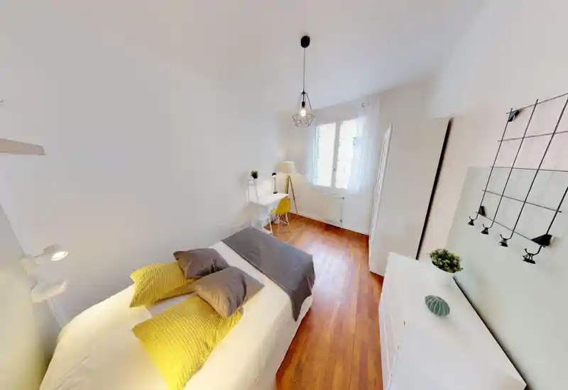 Bright, well-staged bedroom with a double bed, warm wooden floor and a small desk by the window — ideal for a comfortable stay or a rental listing.