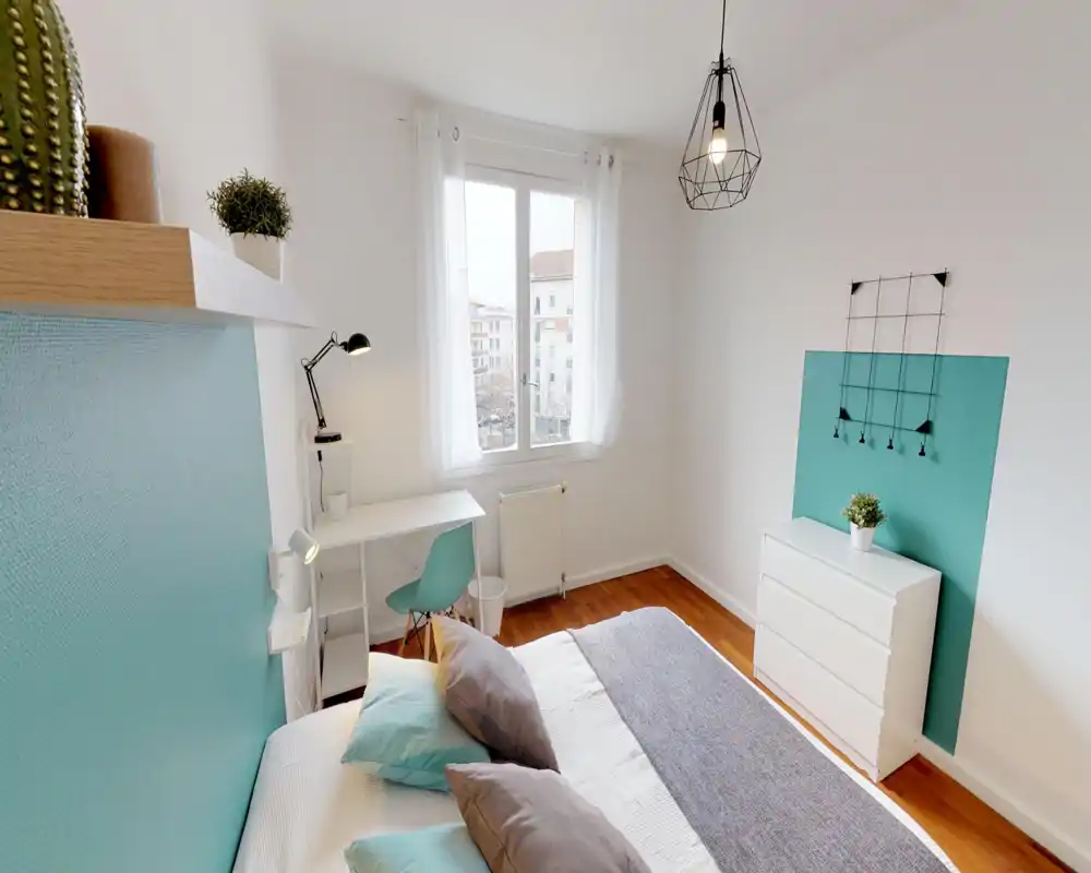 Bright, modern bedroom with a neatly made double bed, coordinating teal accents and a small desk by the window — ideal for a comfortable stay or working-from-home.
