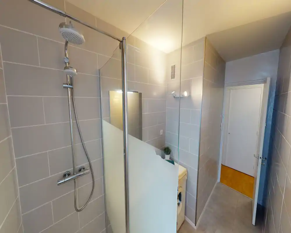 Baño moderno con azulejos, ducha tipo walk-in, mampara de cristal y grifería cromada; tonos neutros y buena iluminación que crean un espacio limpio y funcional.