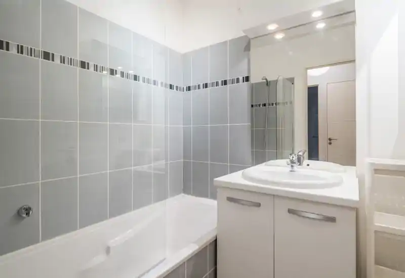 Modern tiled bathroom with a bathtub/shower combination, glass splash screen and a double sink vanity with mirror. Bright, clean and neatly finished space suitable for rental listing.