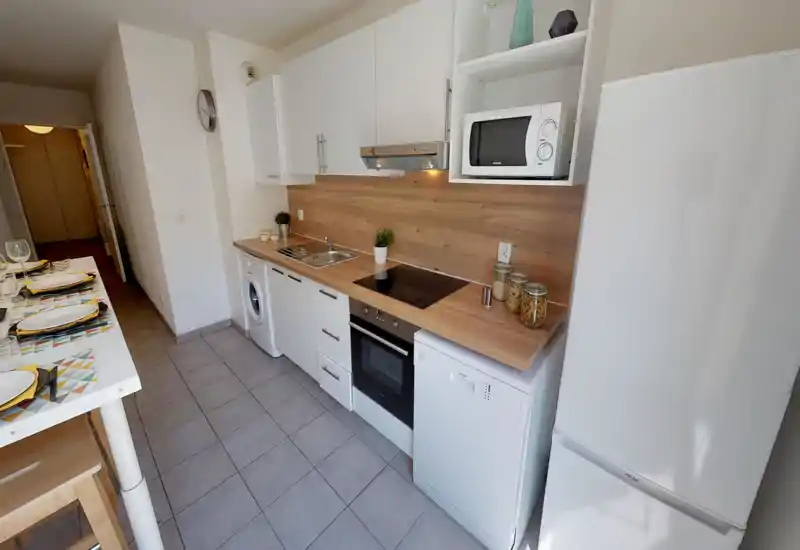 Bright modern kitchen with white cabinets and wood countertops, integrated oven, induction hob, microwave and fridge. A practical breakfast bar is set for dining, and small decorative jars and plants add a warm touch.