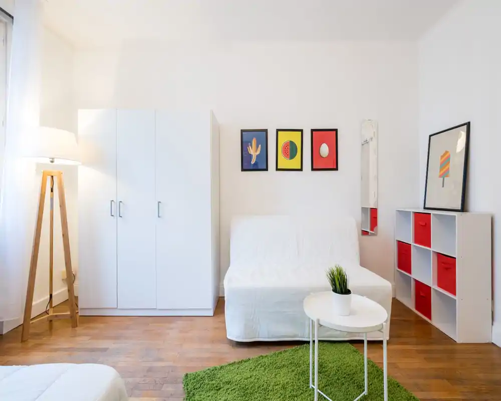 Espace de vie lumineux et minimaliste avec canapé blanc, armoire, cadres décoratifs et tapis vert ; parquet et lampadaire trépied apportent de la chaleur.