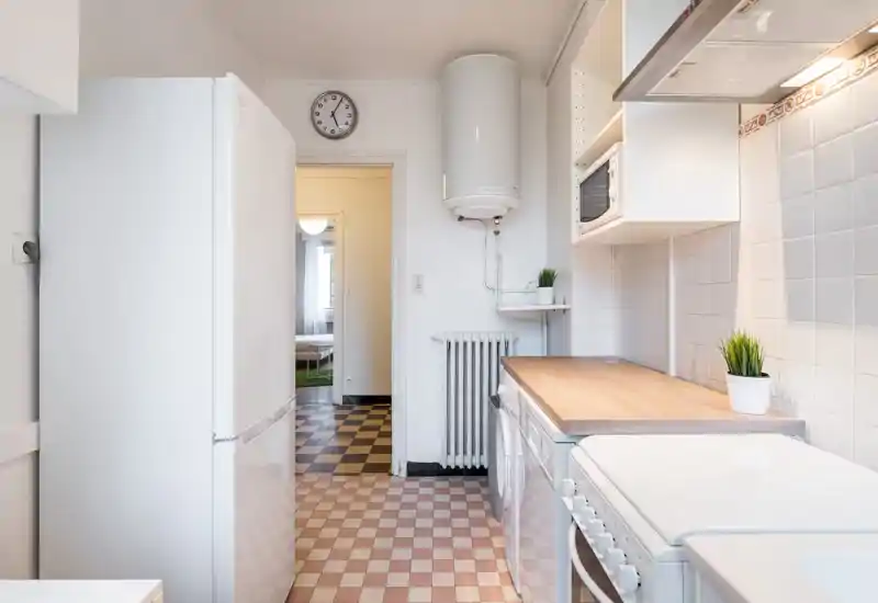 Bright, compact kitchen with white cabinetry, a wooden countertop and tiled backsplash. Functional appliances (fridge, oven, microwave) and small potted plants add a clean, welcoming touch.