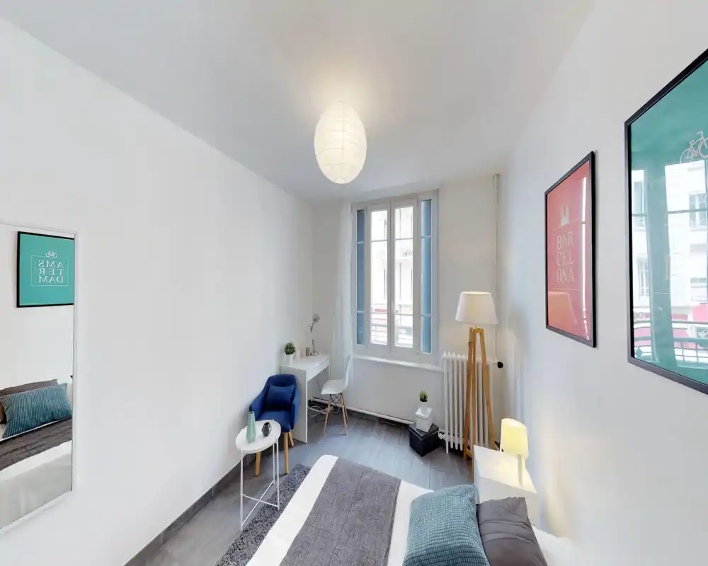 Chambre moderne et lumineuse avec un lit double confortable, lampe de chevet et coussins décoratifs. Un coin bureau et un fauteuil cosy près de la fenêtre ajoutent fonctionnalité et style.