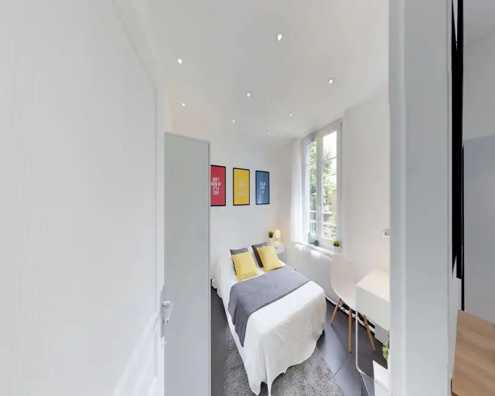 Camera da letto luminosa e moderna con letto matrimoniale centrale, cuscini gialli, comodino e scrivania vicino alla finestra. Ampia finestra che garantisce molta luce naturale e uno stile minimale e fresco.