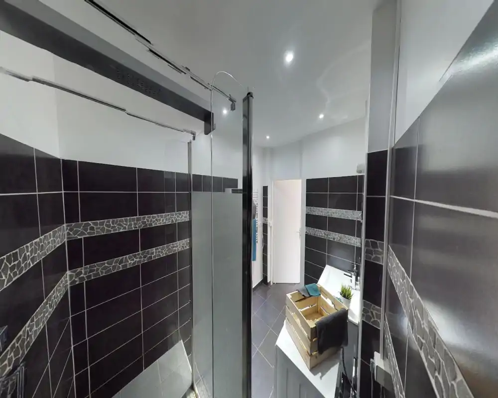 Salle de bains moderne carrelée avec douche à l'italienne, paroi en verre et vasque au style contemporain. Lumineuse et propre, avec des bandes de carrelage décoratives qui apportent une finition soignée.