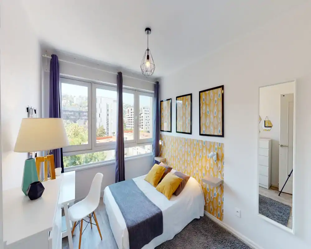 Bright, well-styled bedroom with a double bed, decorative yellow pattern headboard, two mustard pillows and large window providing natural light.
