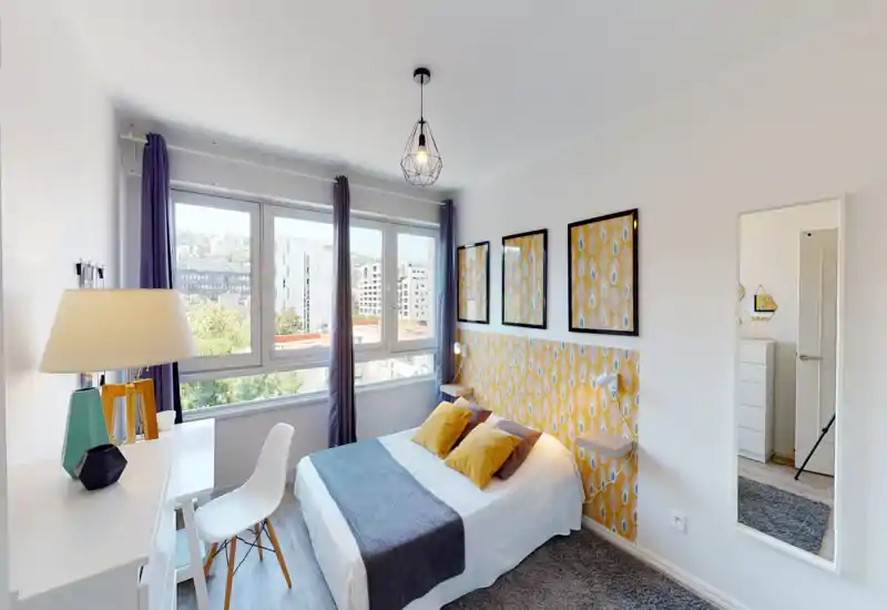 Bright, well-styled bedroom with a double bed, decorative yellow pattern headboard, two mustard pillows and large window providing natural light.