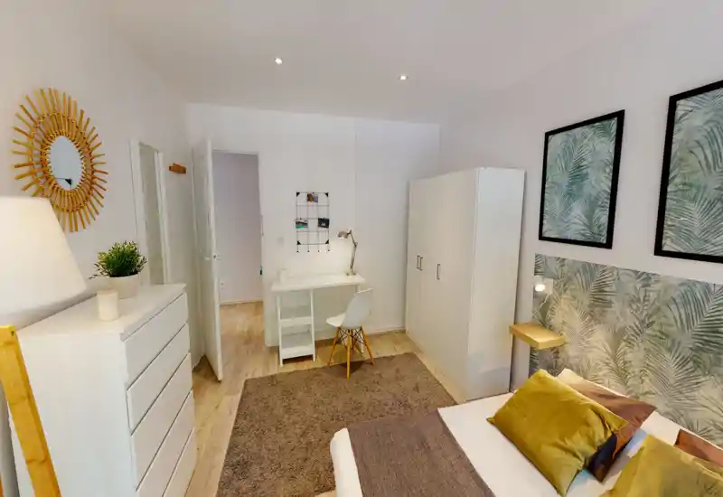 Bright, well-styled bedroom with a comfortable double bed, decorative cushions, a textured headboard and coordinated botanical art. The room includes a wardrobe, desk and chest of drawers — ideal for both rest and remote work.