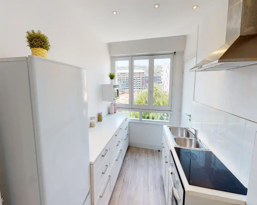 Bright, modern galley kitchen with white cabinets, a ceramic cooktop, double sink and a large window that fills the space with natural light.