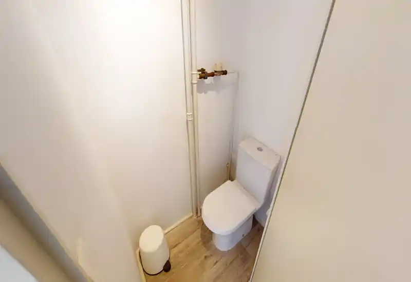 Petit cabinet de toilette avec WC moderne, plomberie apparente et sol effet bois clair ; décoration lumineuse et neutre.