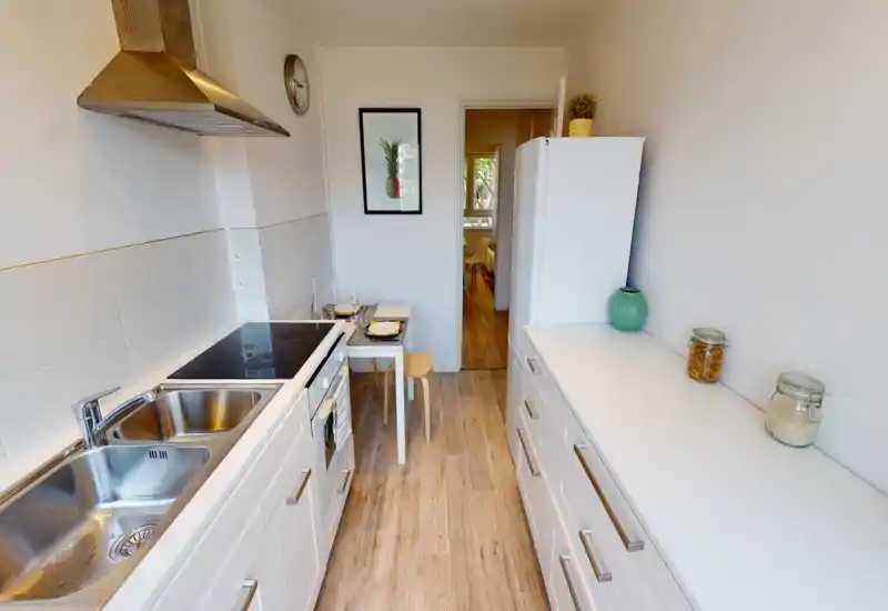 Cucina moderna compatta a corridoio con mobili bianchi, lavello in acciaio, piano a induzione e un piccolo tavolo da pranzo — luminosa e ben arredata, ideale per affitti brevi.